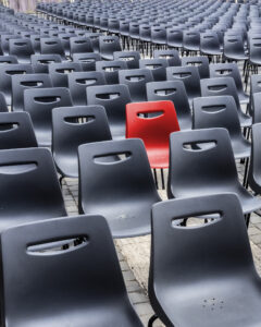 Chaise rouge parmi des chaises noires sur sol pavé Rangée de chaises en plastique noir avec une seule chaise rouge au centre sur sol pavé.