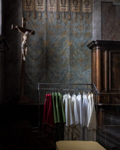 Vêtements liturgiques rouges, verts et blancs suspendus dans une église près d'un crucifix bois. #explos thèmes photo club