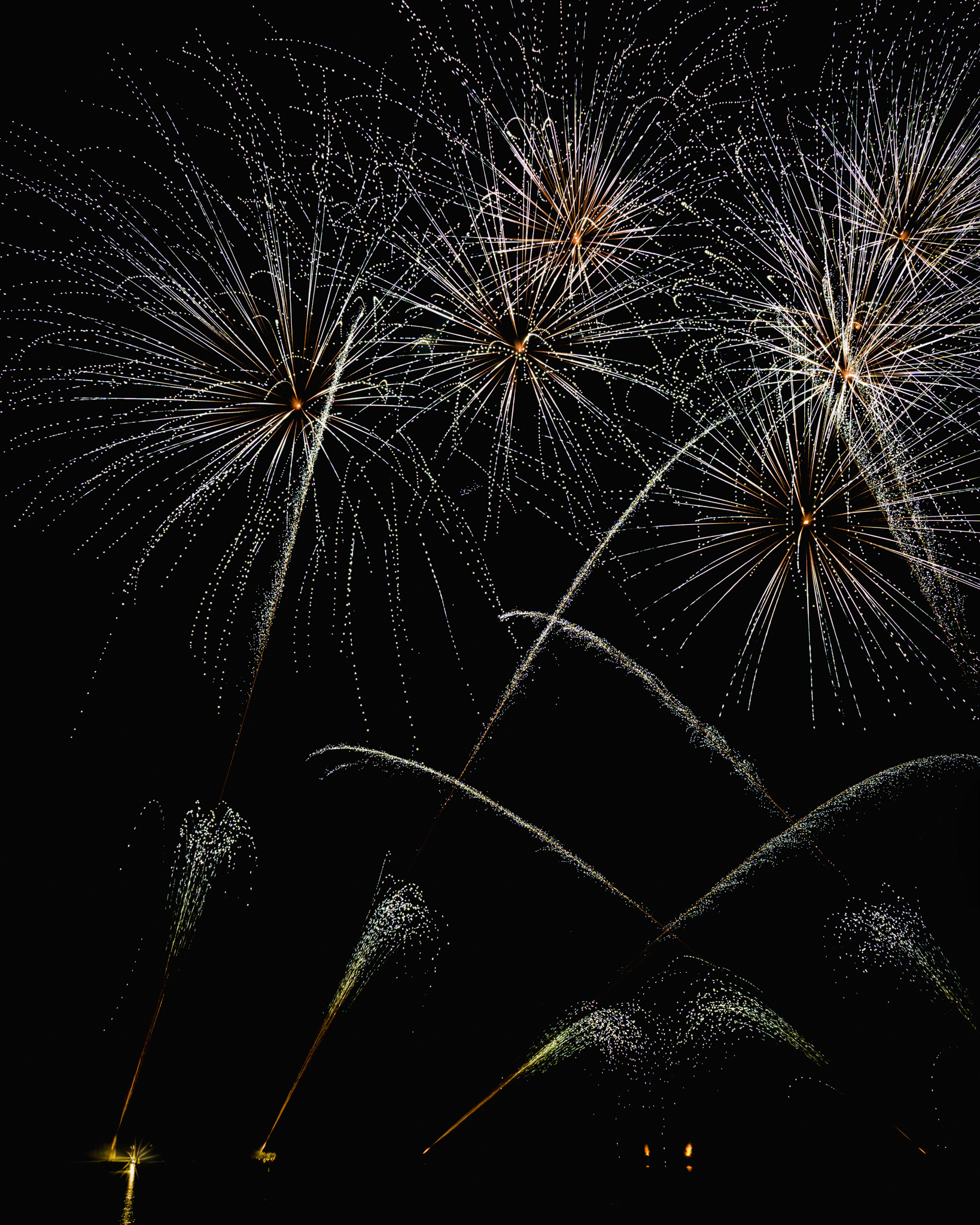 Feux d'artifice lumineux éclatant dans le ciel nocturne avec traînées scintillantes sur fond noir.