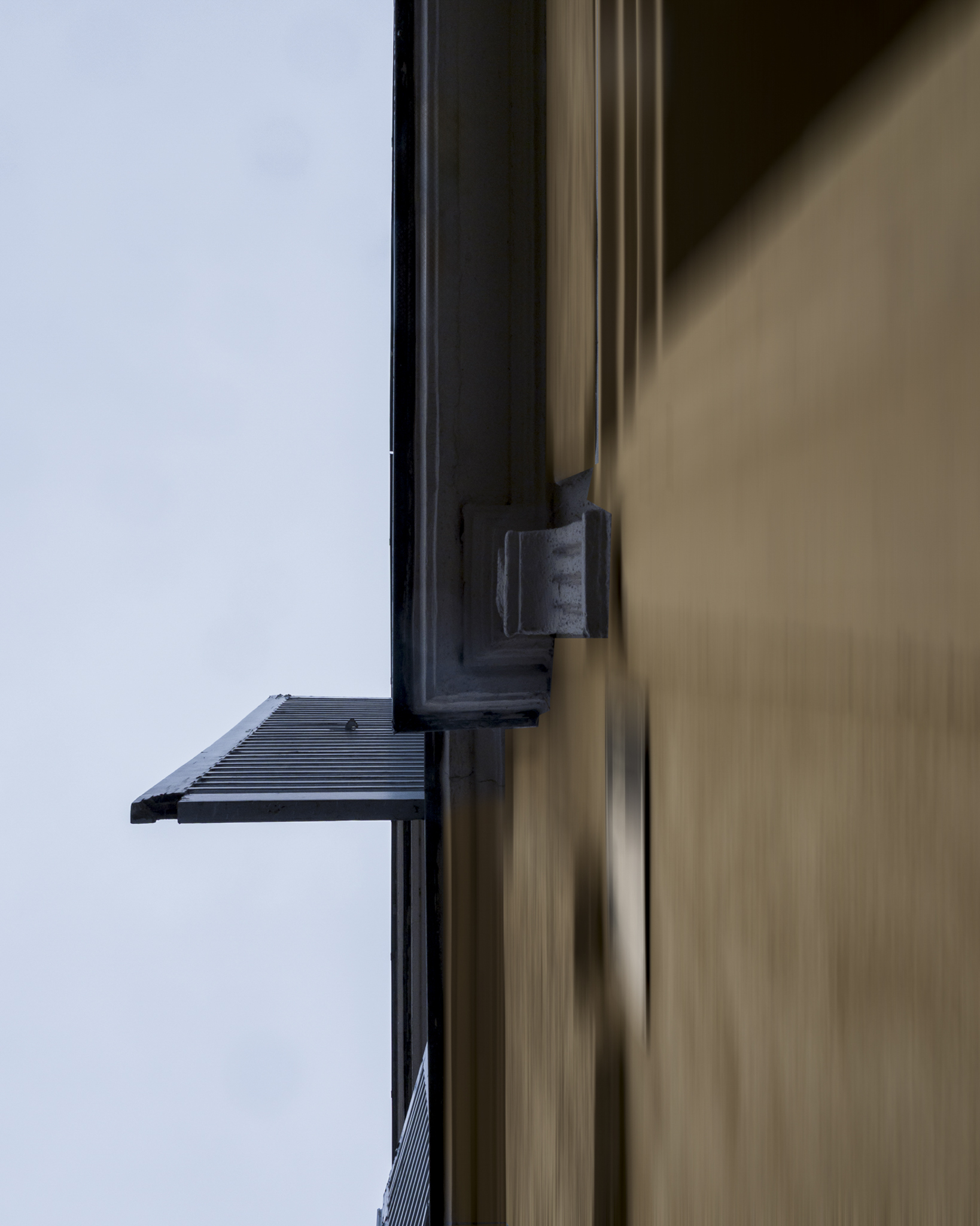 Mur ocre à droite, ferrure grise et plateforme métallique s'étendant vers la gauche; ciel bleu.