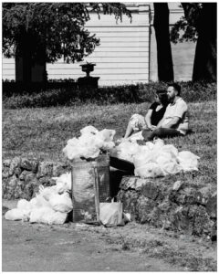 Couple assis dans un parc près d'une poubelle débordant de sacs plastiques jaunes. #explos thèmes photo club
