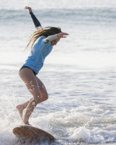 Personne en tenue de surf glissant sur une planche au-dessus de l'eau avec les bras écartés.