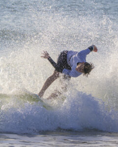 Surfeur en combinaison blanche et noire effectuant une figure sur une vague éclaboussante.