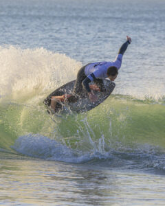 Surfeur en combinaison réalisant une figure sur une vague verte dans la mer calme.