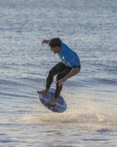 Homme en combinaison bleue effectuant un saut sur une planche sur l'eau.