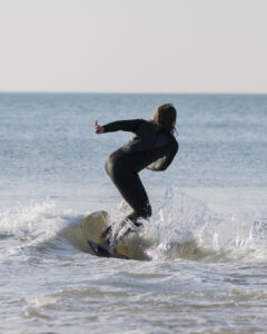 Personne en combinaison de surf debout sur une planche sur une petite vague près du rivage.