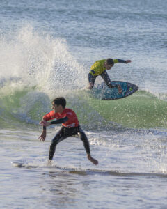 Deux surfeurs en combinaisons rouge et jaune surfant sur des vagues à proximité du rivage.