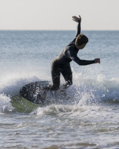 Surfeur en combinaison noire glissant sur une petite vague avec éclaboussures d'eau.