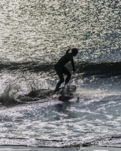 Personne silhouettée surfant sur une vague avec éclats de lumière sur l'eau.